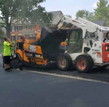 Skid loader dumping asphalt it into paving machine hopper